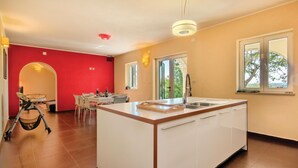 Een moderne keuken met een centraal eiland, een eethoek met een rode accentmuur, en grote ramen die zorgen voor natuurlijk licht.