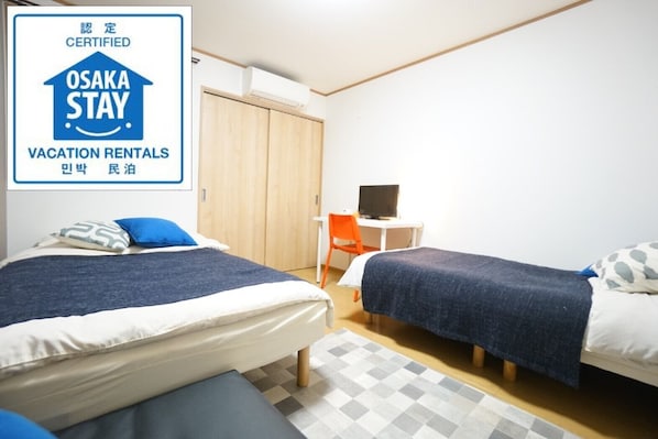 A room with two beds, a desk, and a chair. There is a sign indicating certified vacation rentals.