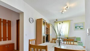 A dining area with a table set for four, wooden chairs, a vase with flowers, and a clock on the wall. - Lovely apartment for 5 people with pool, A/C, WIFI, TV, balcony and pets allowed (Zadar)