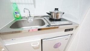 A compact kitchenette with a stainless steel sink, a pot on the stove, and a dishwasher below. - Terry's Apartment Namba South V C01F (Osaka)