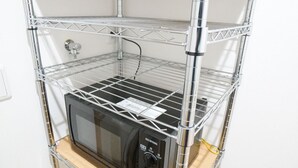 A metal wire shelving unit with a microwave on the bottom shelf. - Terry's Apartment Namba South V C01F (Osaka)