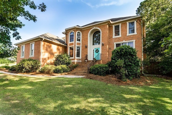 A two-story brick house with a front porch, a green door, and a wreath on the door.