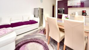 Un salon moderne avec un canapé blanc, une table à manger et des chaises, un coin cuisine avec des meubles violets et un réfrigérateur.
