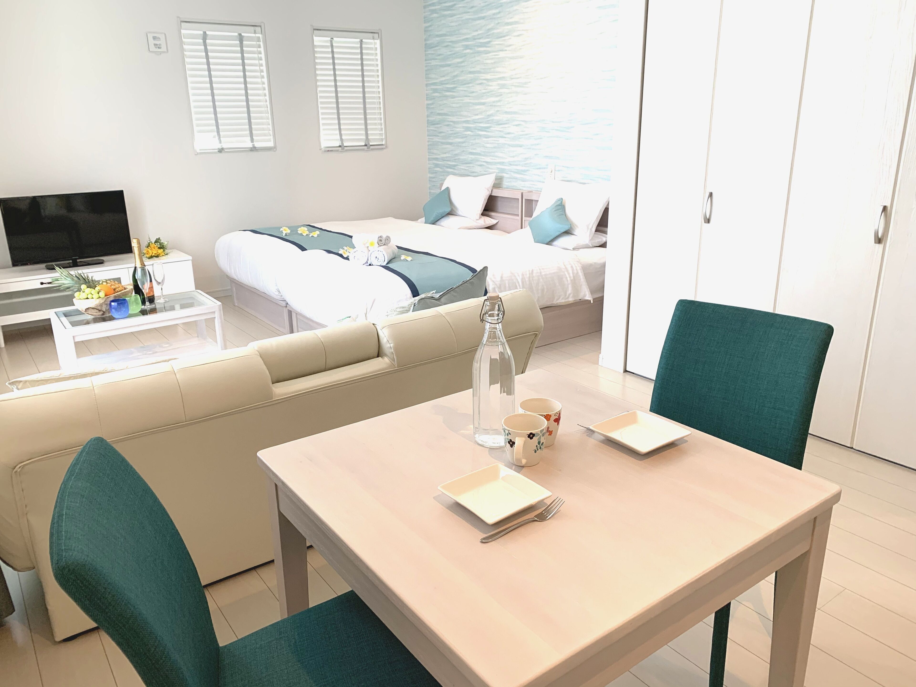A modern hotel room with a sofa, a dining table, a TV, and a bed with a view of the sea.
