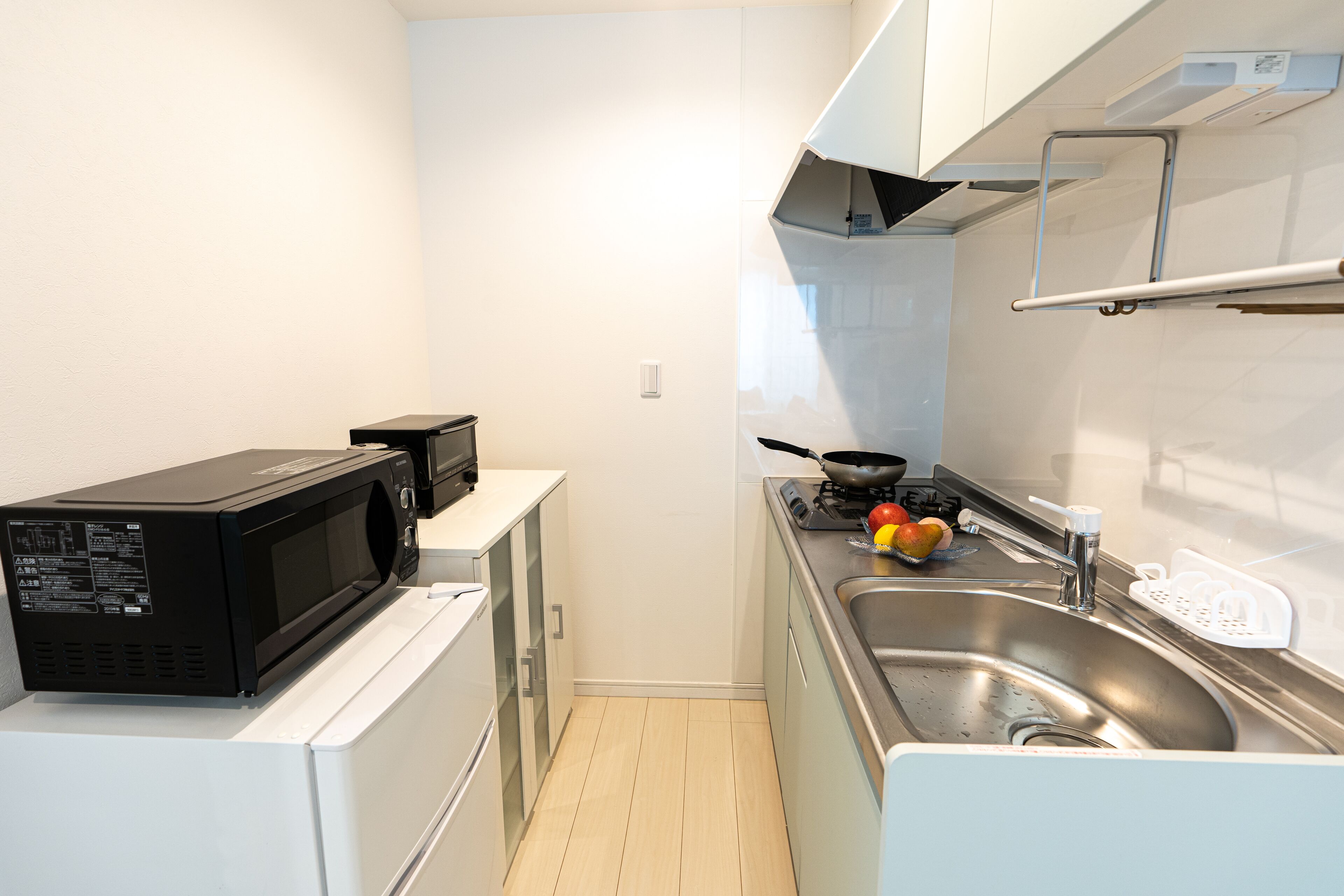 Una cocina compacta equipada con microondas, estufa, lavabo y armarios blancos.
