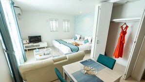 A modern hotel room with a sofa, a dining table, a TV, a bed, and a wardrobe. - Ecot Kugai 1 (Miyakojima)