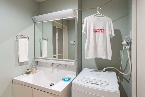 A bathroom with a white sink, a mirror, a white towel, a white t-shirt hanging on the wall, and a washing machine.