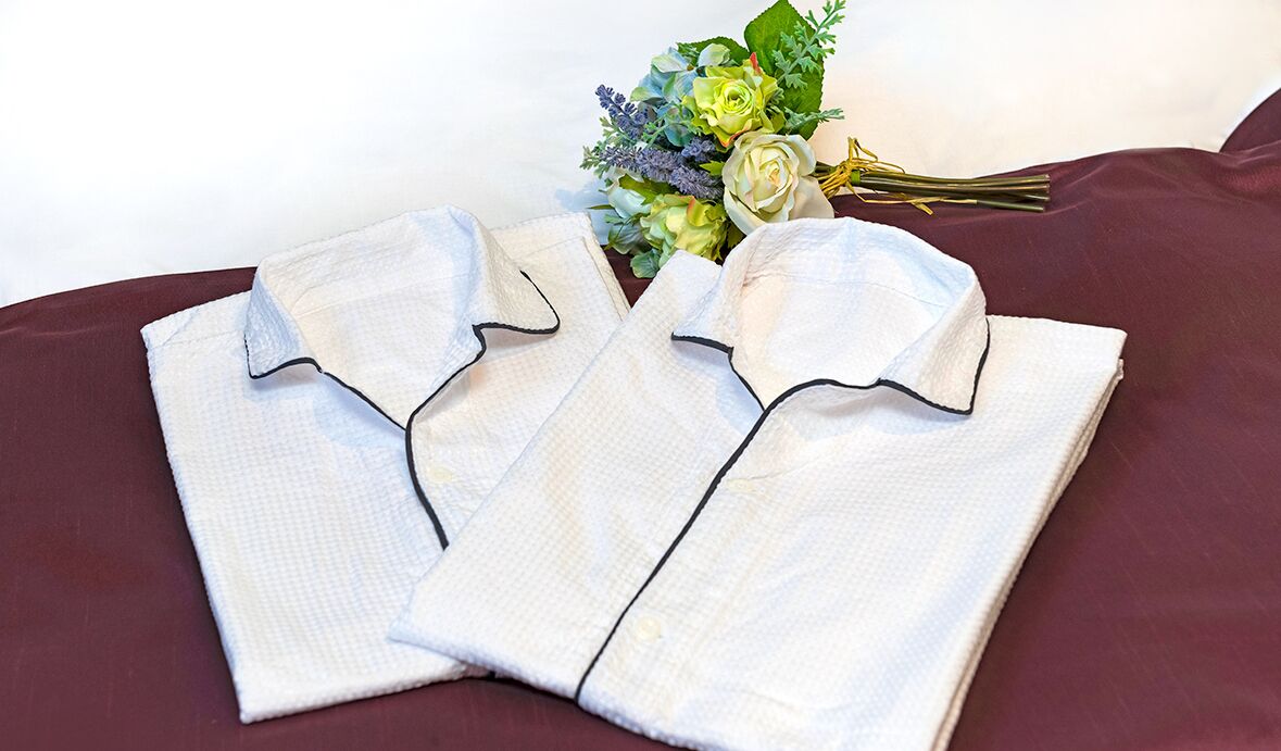 Two neatly folded white shirts with black trim on a dark red bedspread.