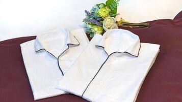 Two neatly folded white shirts with black trim on a dark red bedspread.