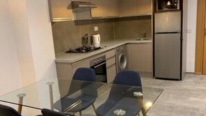 A modern kitchen with a glass dining table and chairs, a built-in oven, and a stainless steel refrigerator. - Vision immo (Saint-Ouen)