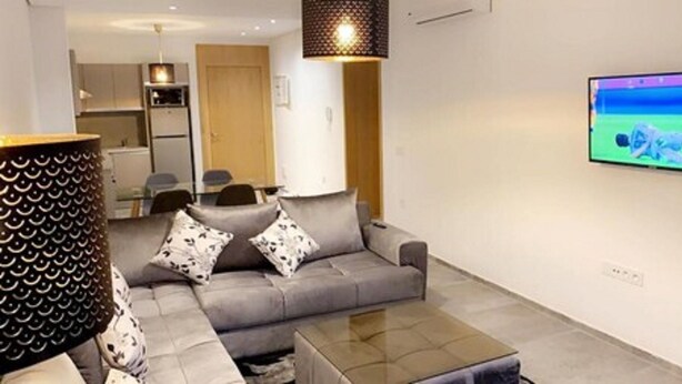 A modern living room with a grey sofa, a coffee table, and a flat-screen TV mounted on the wall. - Vision immo (Saint-Ouen)