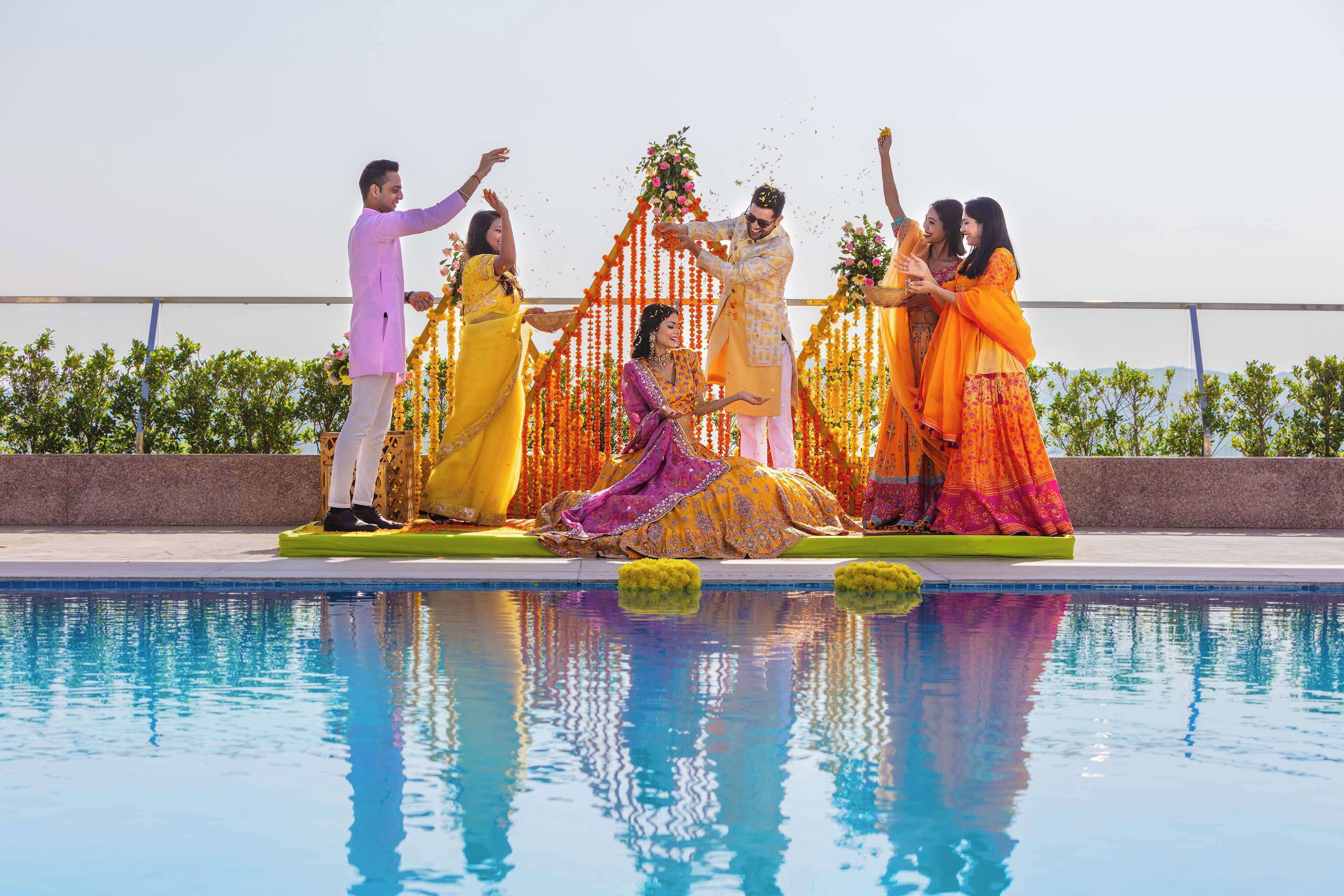 A group of people standing by a pool with a decorative arch and flowers.