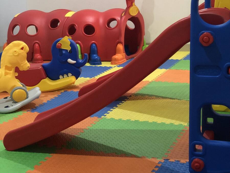 Zona de juegos infantiles con un tobogán, colchonetas de colores y diversos juguetes.