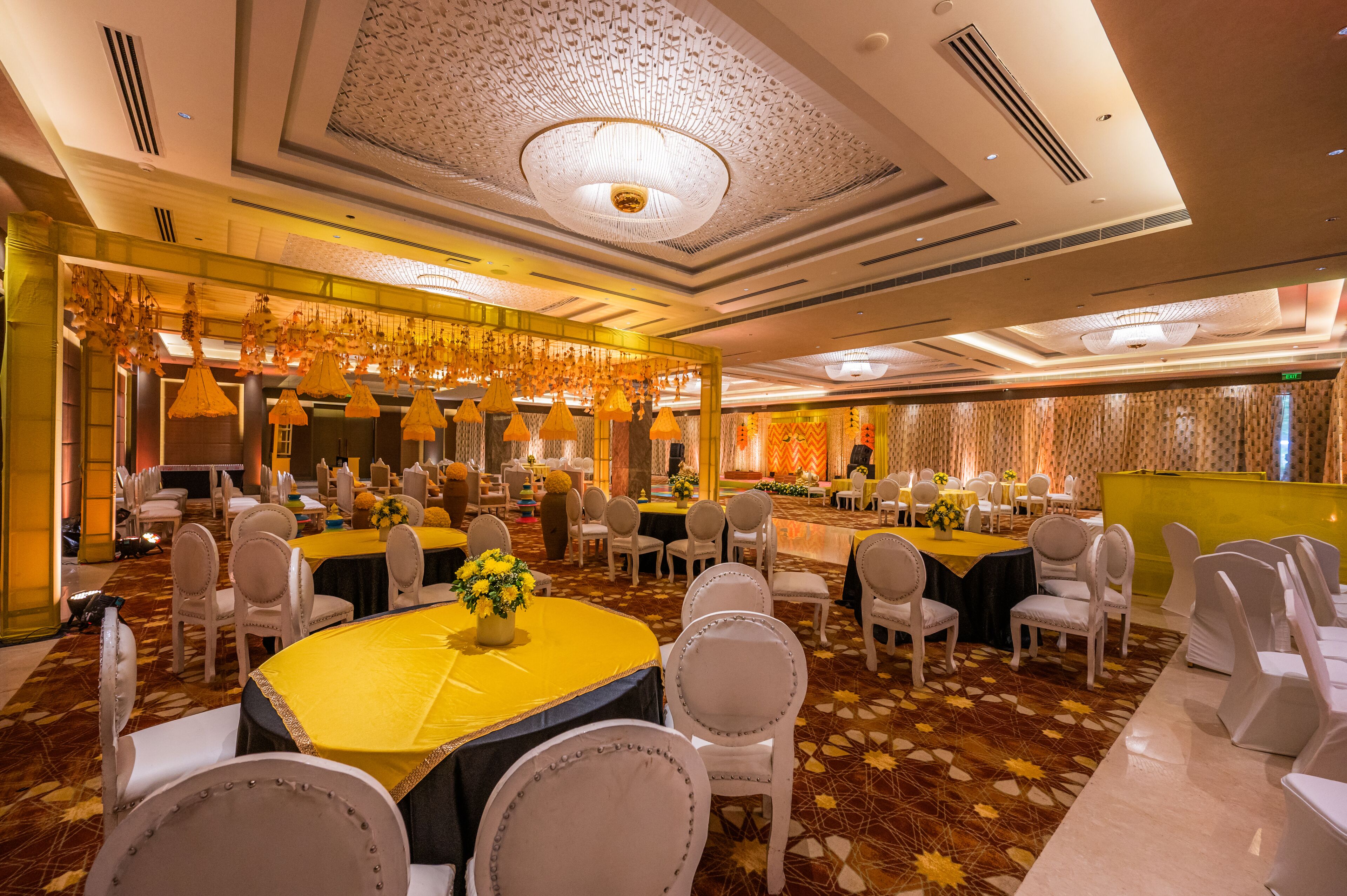 Un salón de banquetes con mesas redondas, sillas blancas y una alfombra estampada.