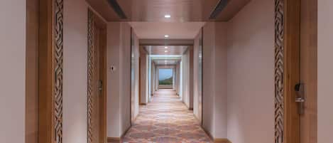 A long, narrow hallway with patterned carpet, wooden doors with decorative panels, and recessed lighting.