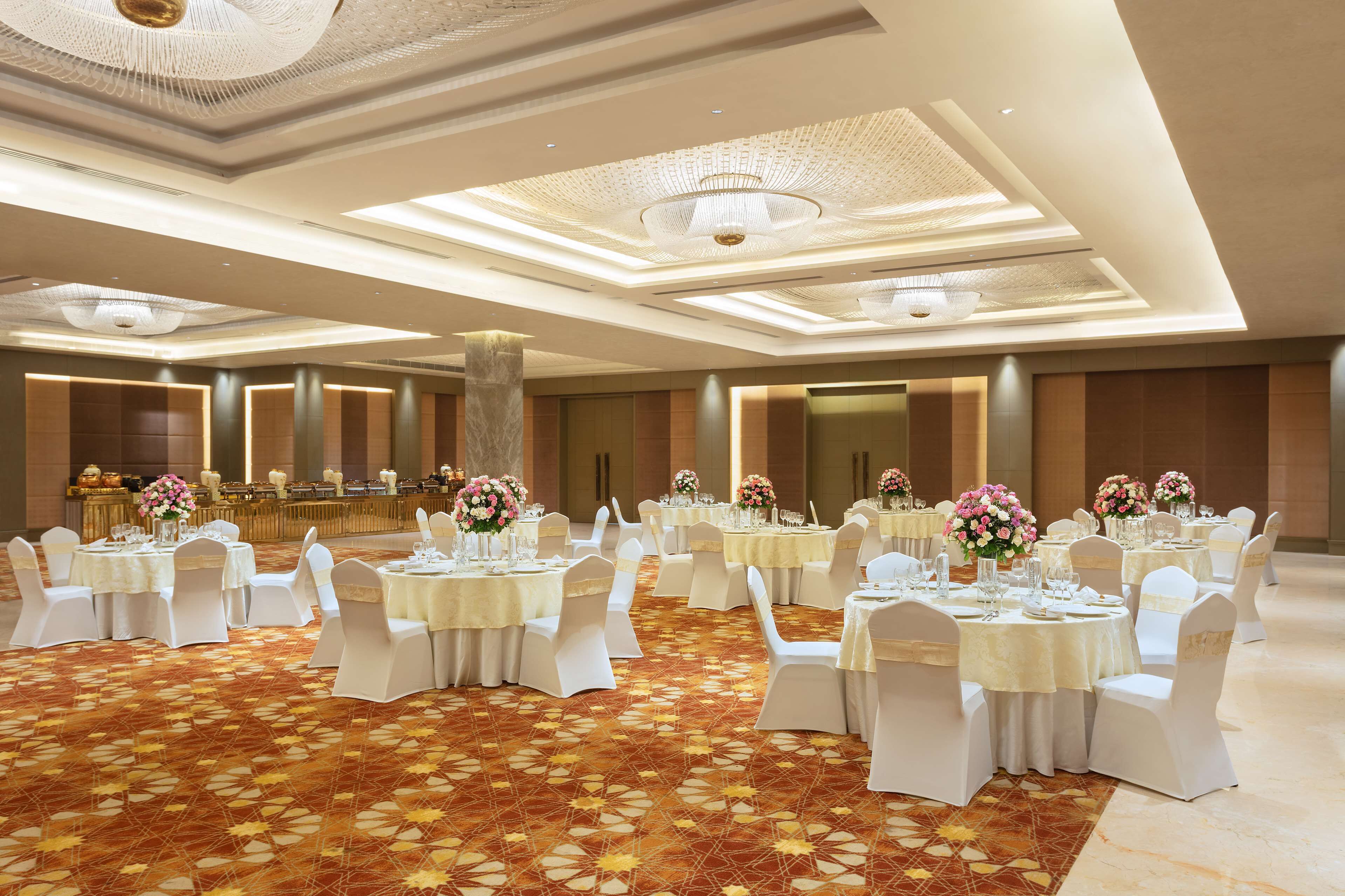 Une salle de banquet avec des tables rondes, des chaises blanches et des centres de table ornés de fleurs.