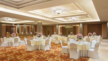 Un salón de banquetes con mesas redondas, sillas blancas y centros de mesa florales.