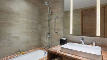 A bathroom with a marble countertop, a white sink, a shower with a handheld showerhead, and a wooden cabinet.