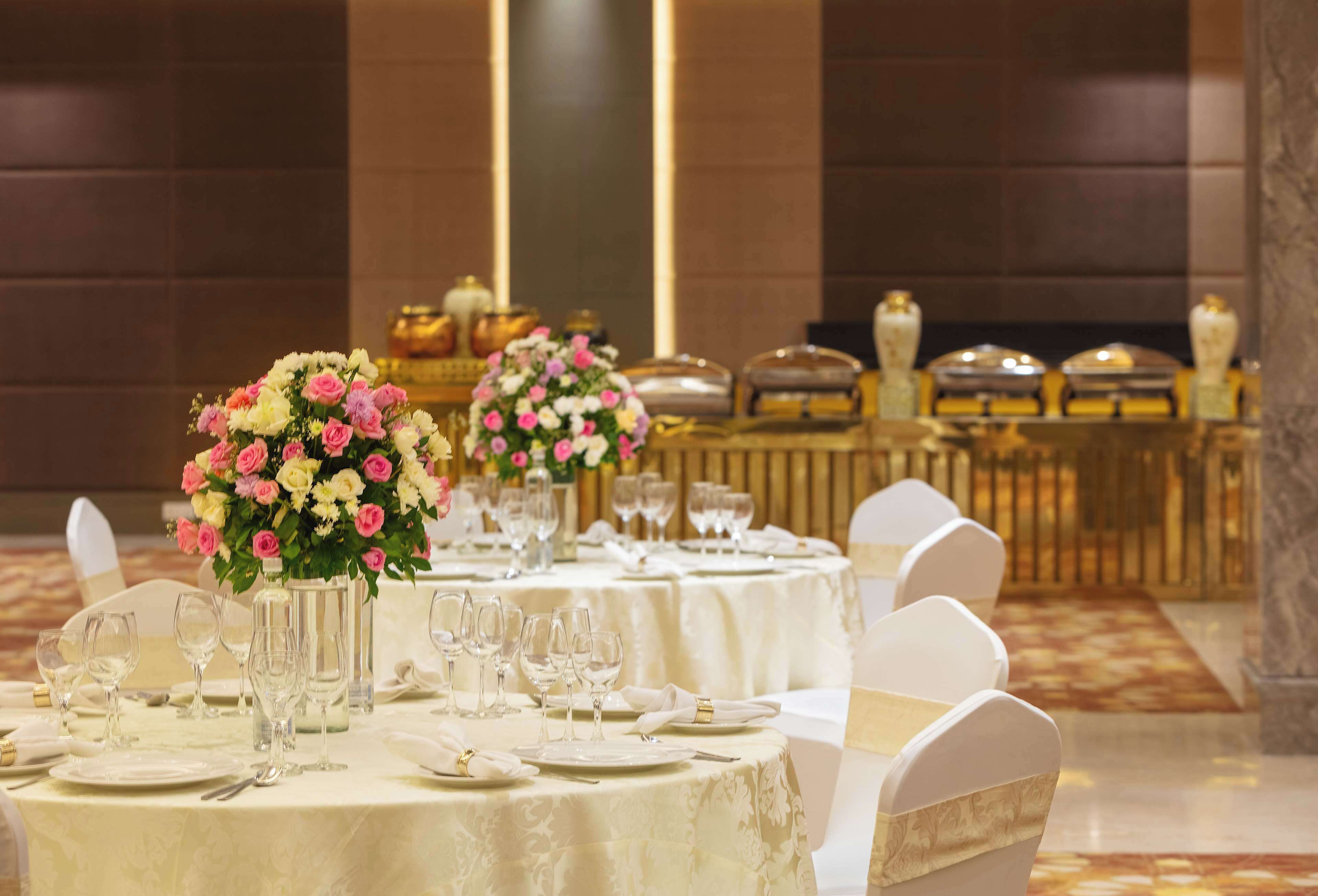 A banquet hall with round tables set for dining, each with white tablecloths, glassware, and plates.