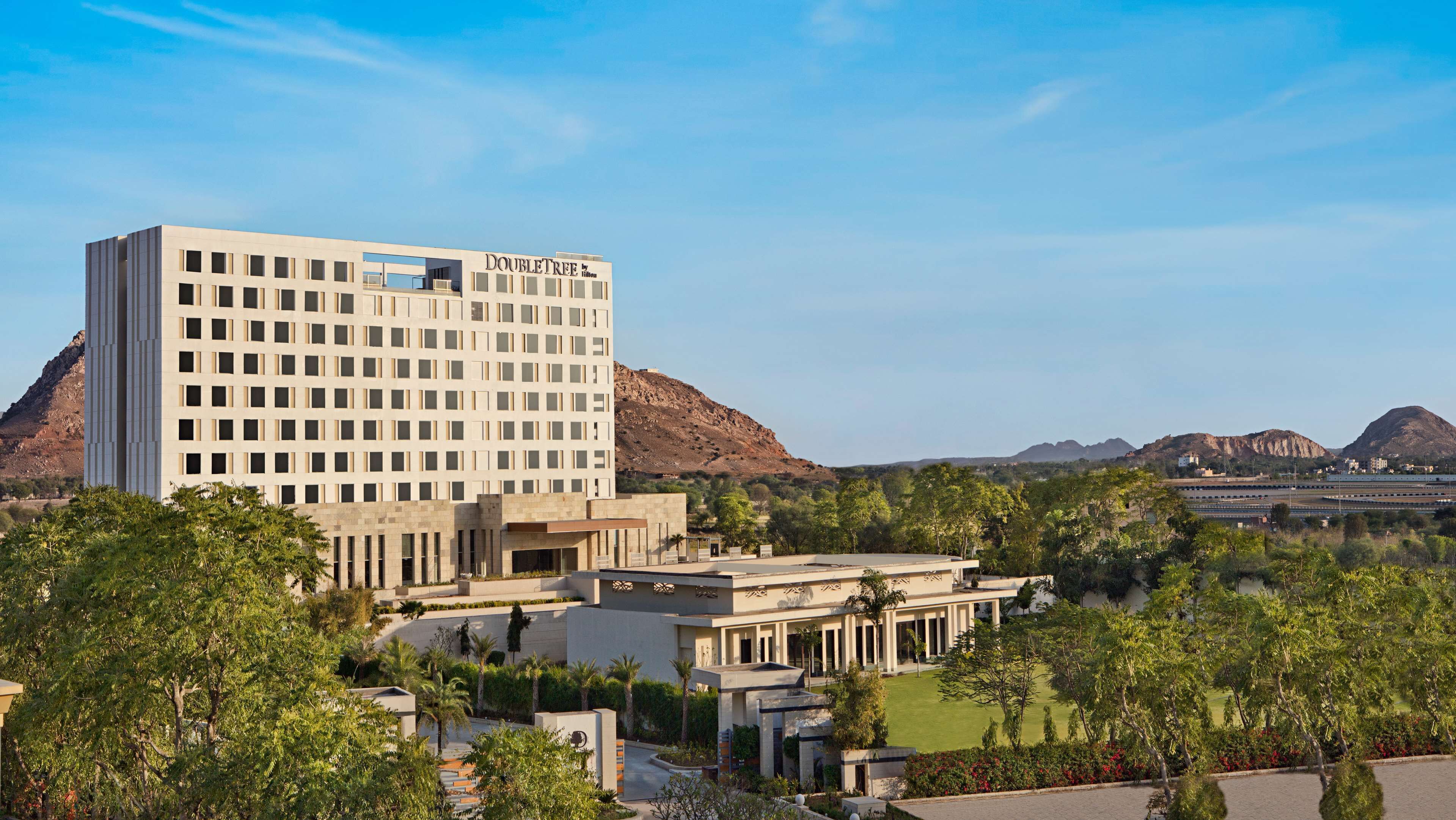 Ein modernes Hotel mit einem gut sichtbaren "DOUBLETREE by Hilton" Schild, umgeben von üppiger Vegetation und Bergen im Hintergrund.