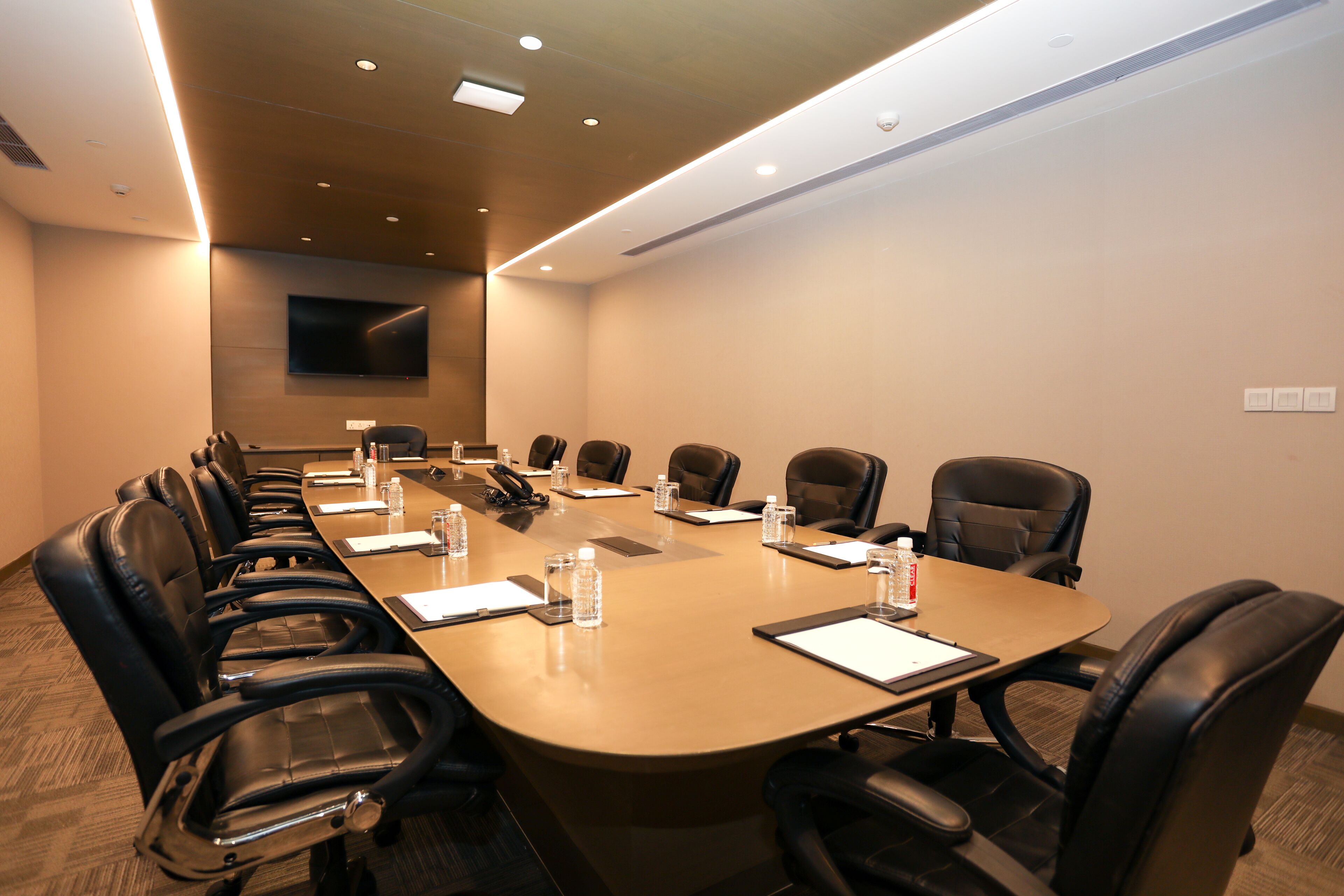 A conference room with a long table, multiple chairs, water bottles, and a flat-screen TV on the wall.