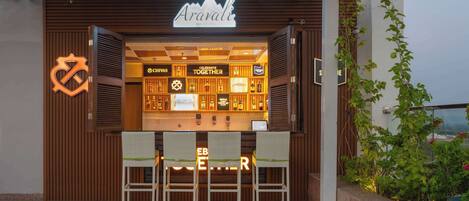 Un bar y restaurante llamado Aravali, con fachada de madera, una variedad de botellas de licor y mesas al aire libre.