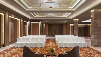 A spacious conference room with rows of white chairs, a chandelier, and a patterned carpet.