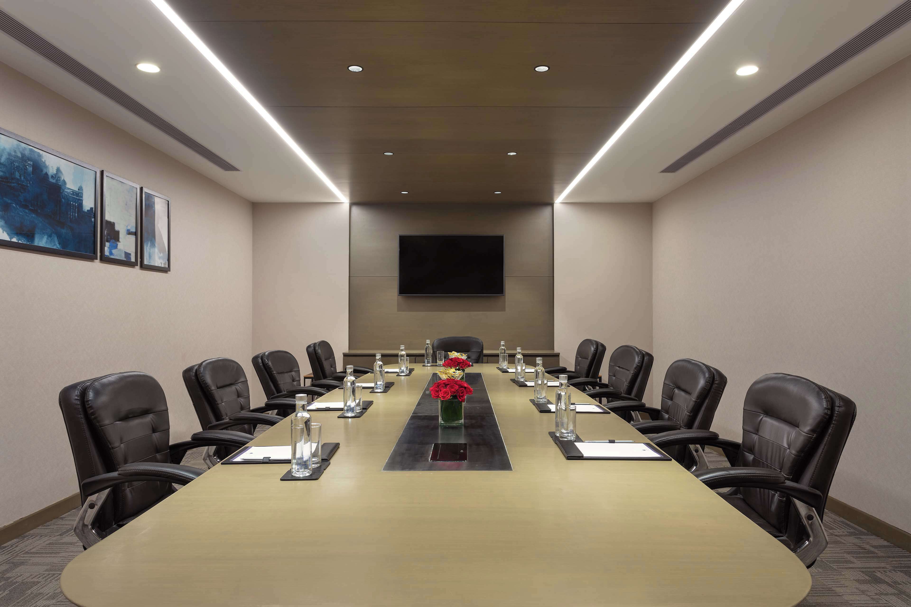 Un salón de conferencias con una larga mesa, sillas, un televisor de pantalla plana y cuadros en la pared.
