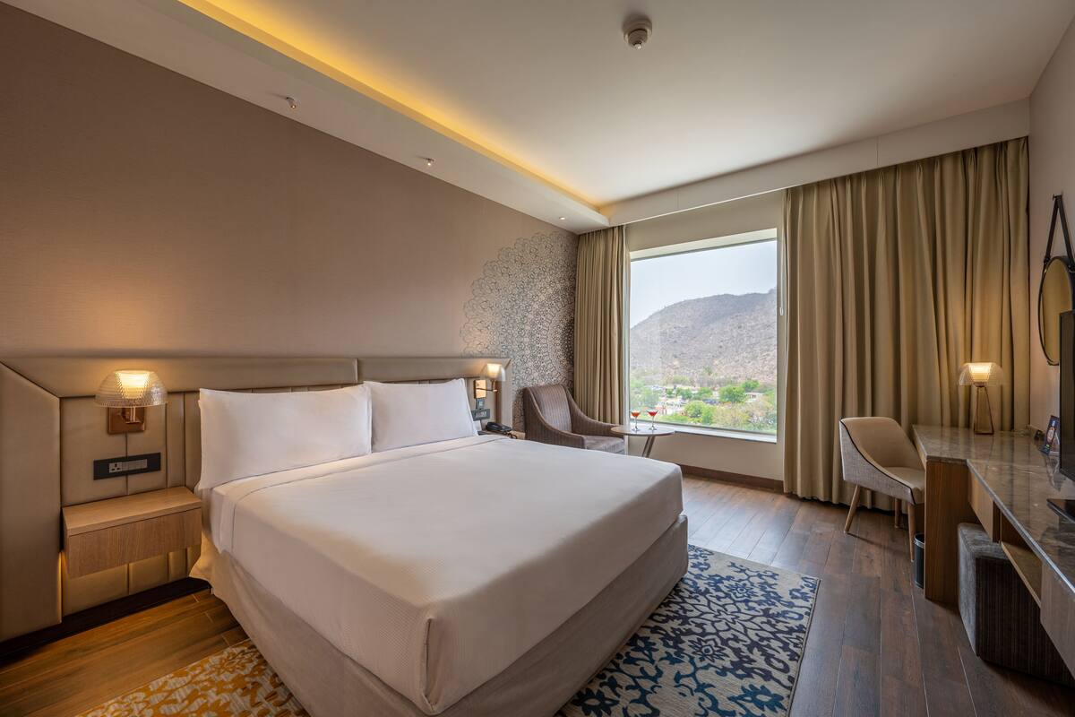 Habitación de hotel con una cama grande, un escritorio, una silla y vistas a la montaña.