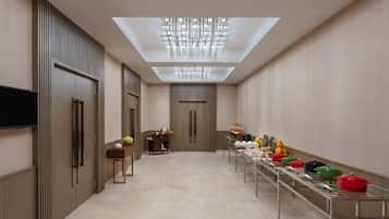 Un couloir d’hôtel moderne, avec une longue table où sont exposés des pots colorés, un téléviseur à écran plat fixé au mur et un luminaire au plafond.