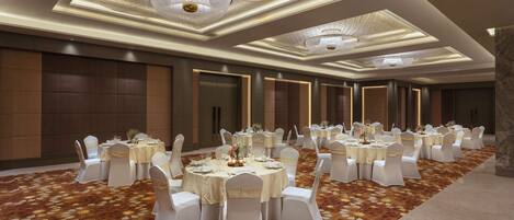 Un salón de banquetes con mesas redondas, sillas blancas y candelabros.