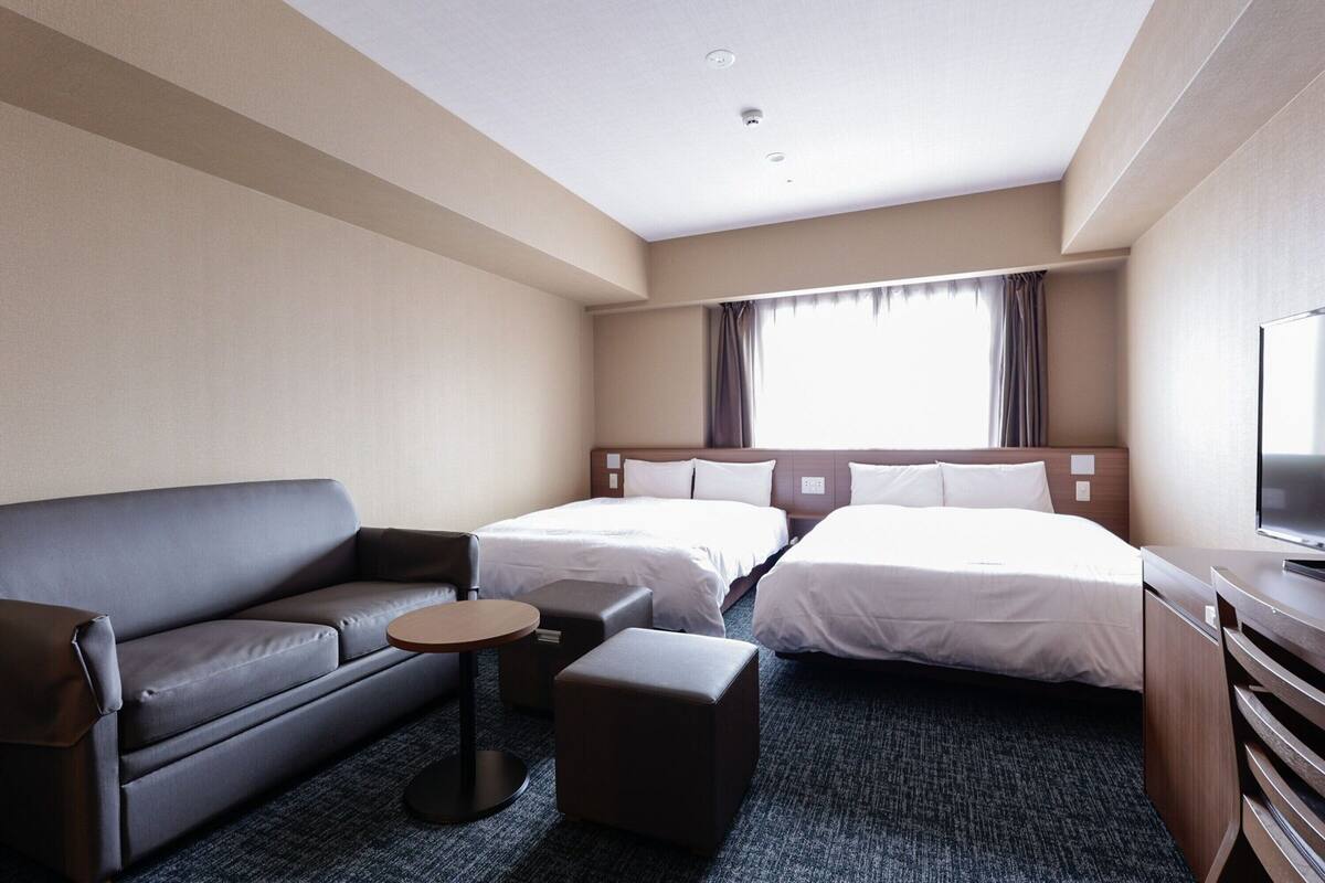 A hotel room with a sofa, two single beds, a small round table, and a TV.