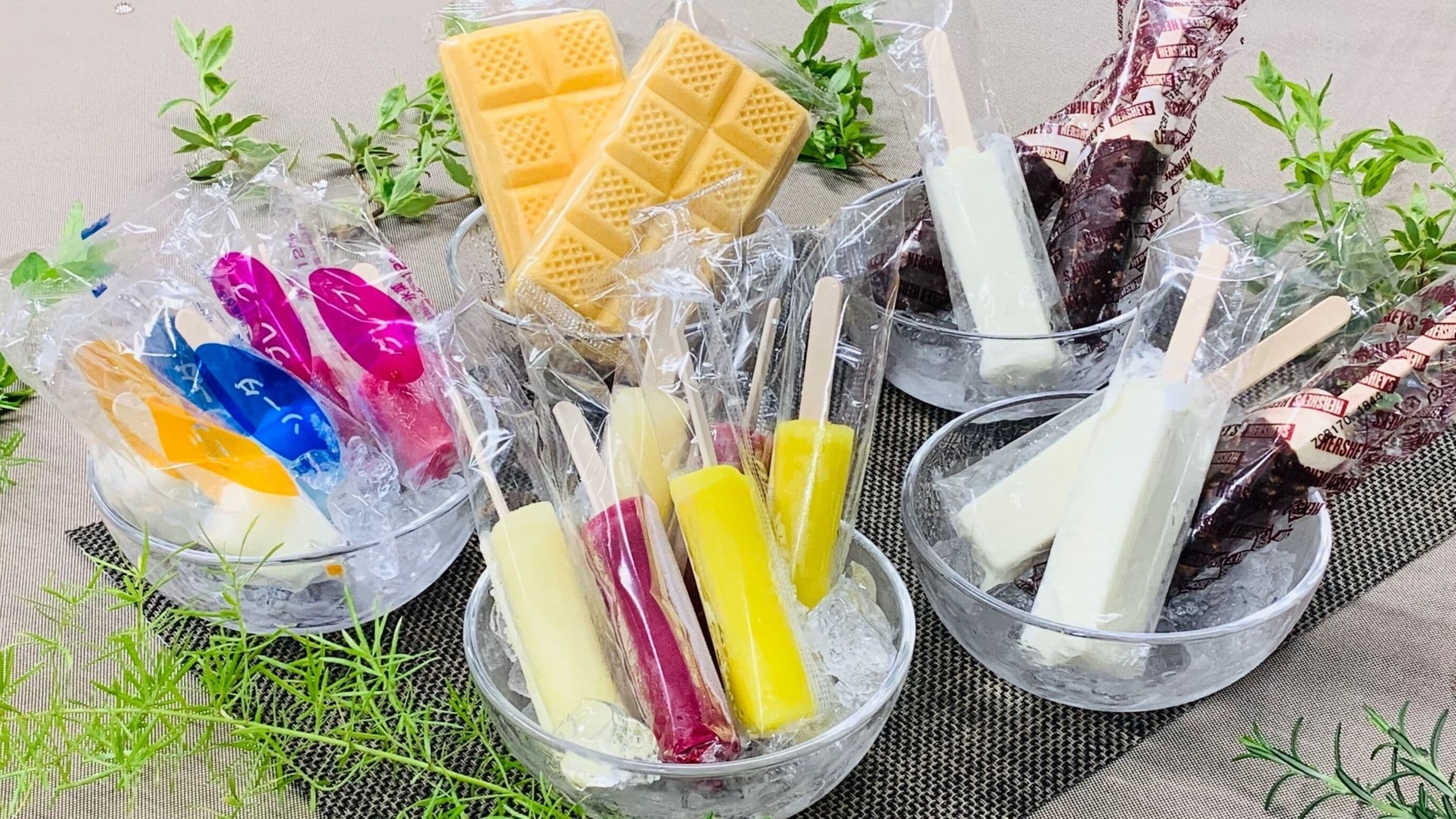 Various ice cream bars and a waffle in clear plastic cups on a table with a woven mat.
