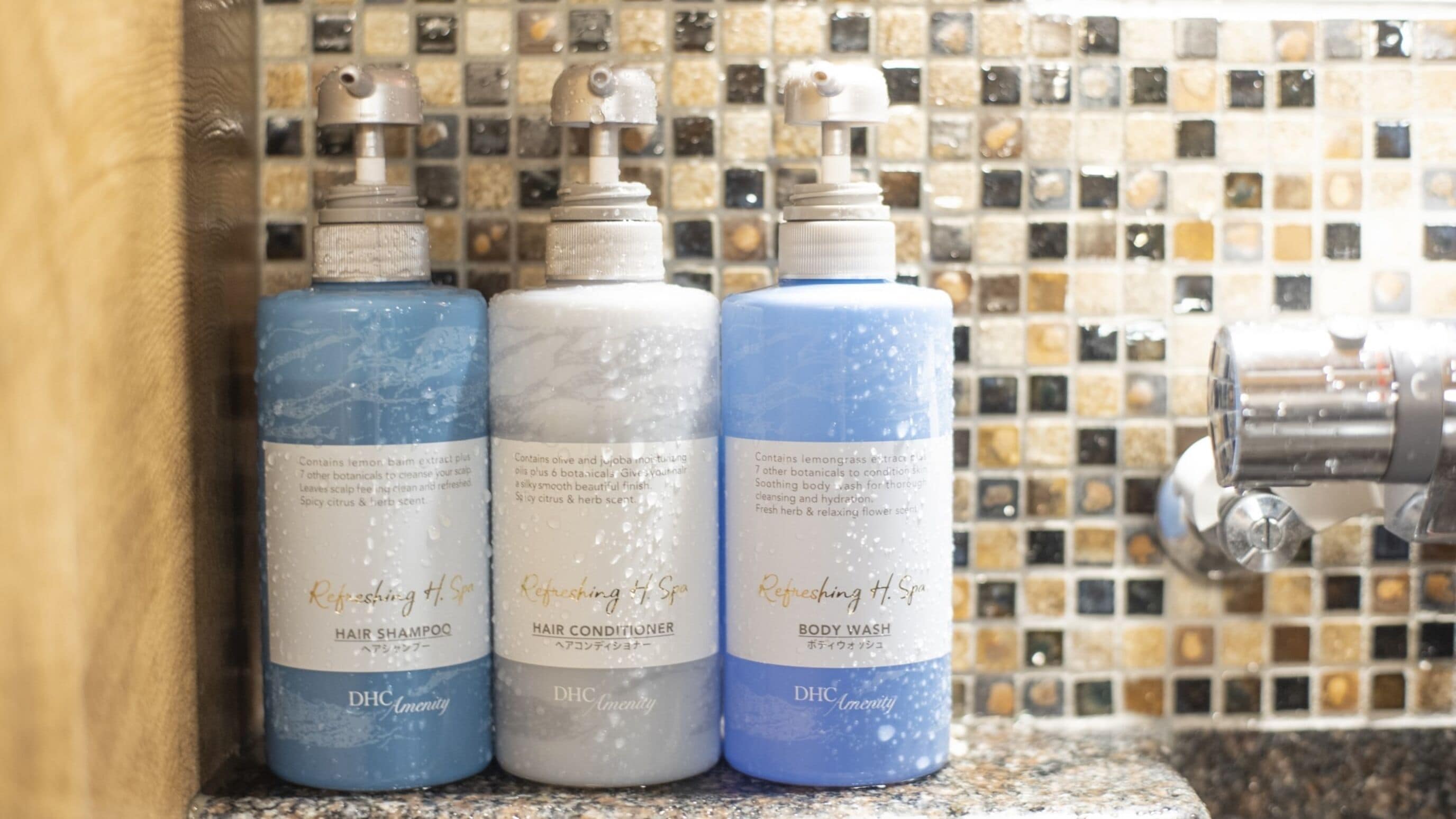 Tres botellas de productos para el cabello DHc Amenity sobre una encimera de baldosas.