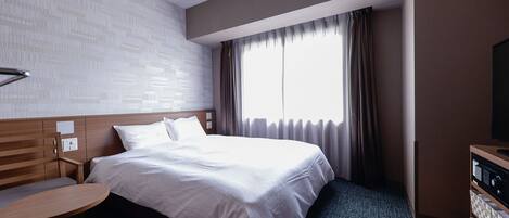 A hotel room with a large bed, a wooden headboard, a small round table, a television, and a window with curtains.