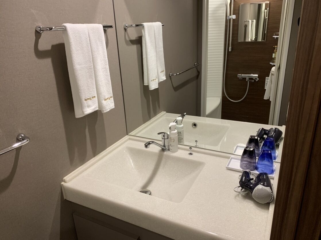 A bathroom with a white sink, two towels hanging on a rack, a mirror, and a shower area.