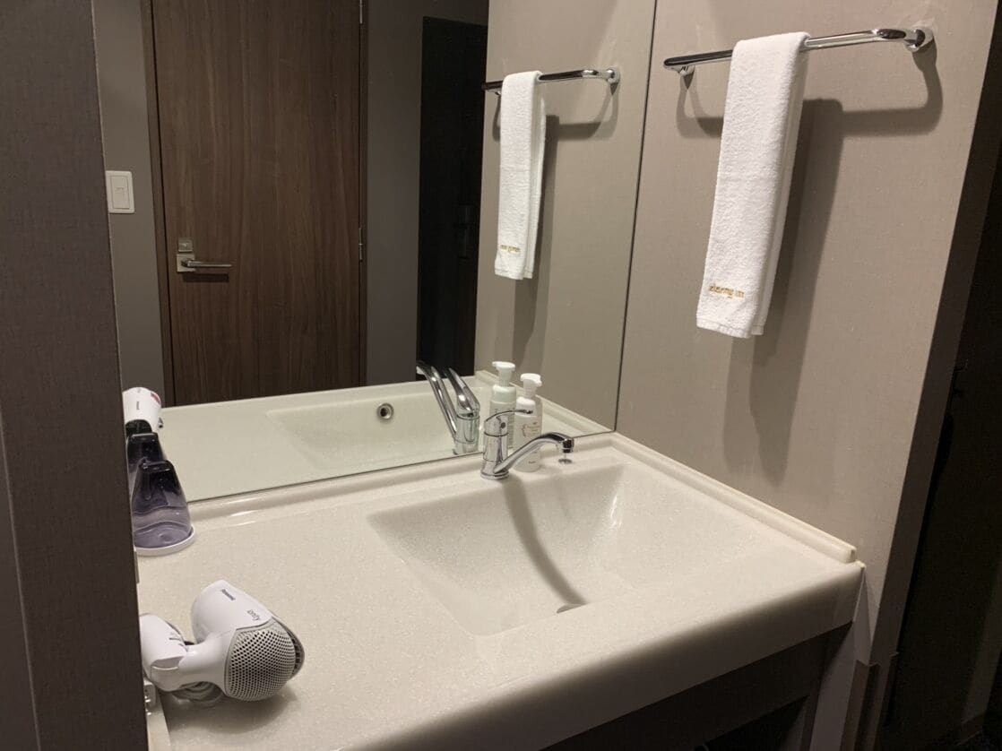 A bathroom with a large mirror, a sink, a hairdryer, and two towels hanging on towel bars.