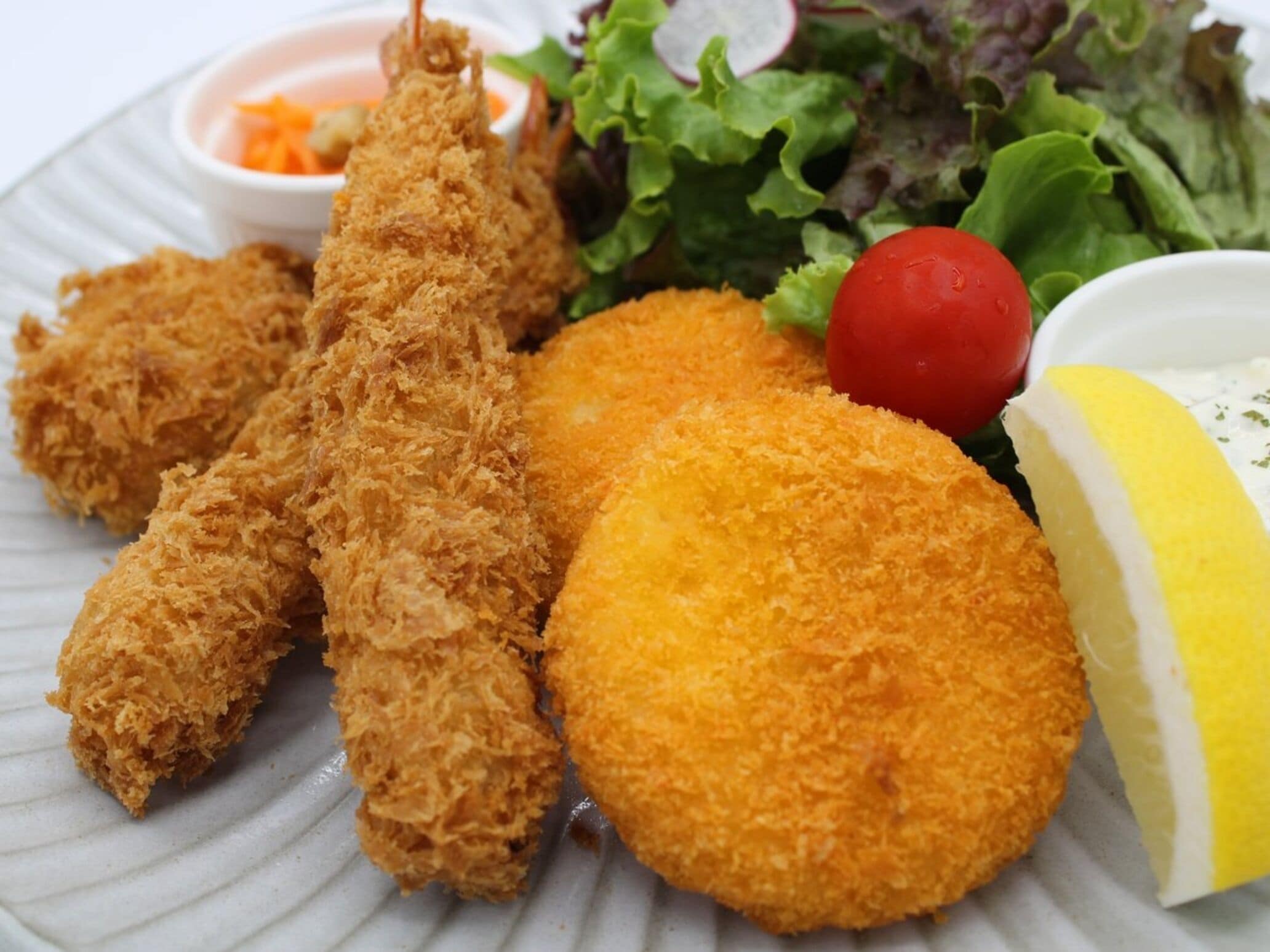 A plate with breaded and fried items, a lemon wedge, and a small salad with a cherry tomato.
