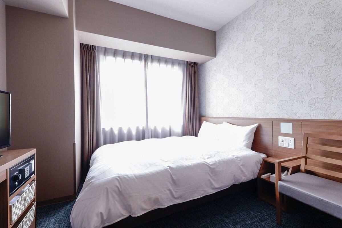 A hotel room with a large bed, a wooden nightstand, a television, and a window with curtains.