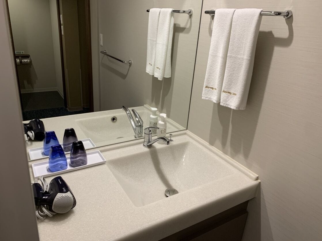A hotel bathroom with a large sink, a mirror, and several toiletries on the counter.