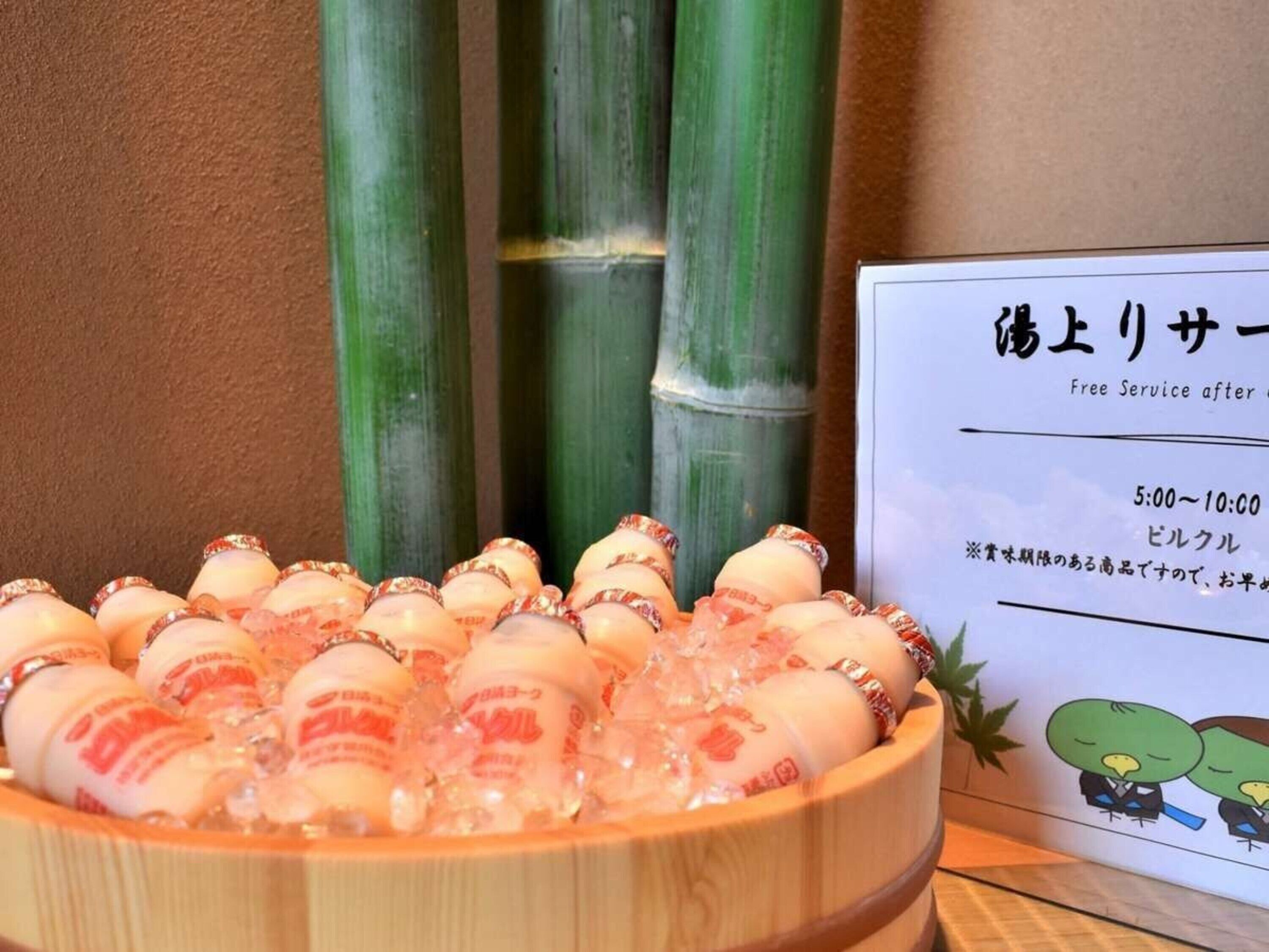 A wooden bowl filled with ice and bottles of a beverage, with a sign in the background indicating a free service after 5:00-10:00.