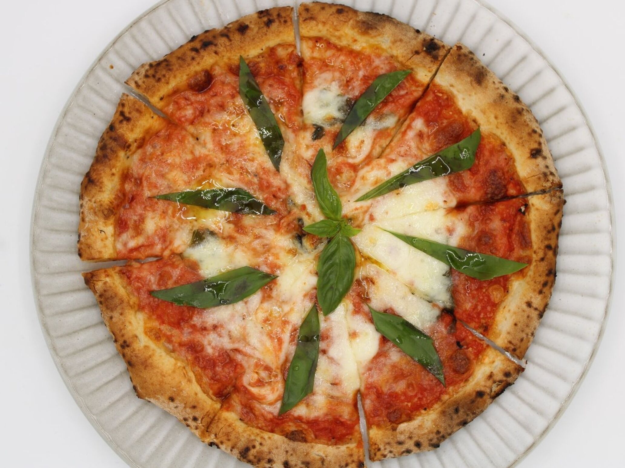 A pizza on a white plate with a ribbed edge.