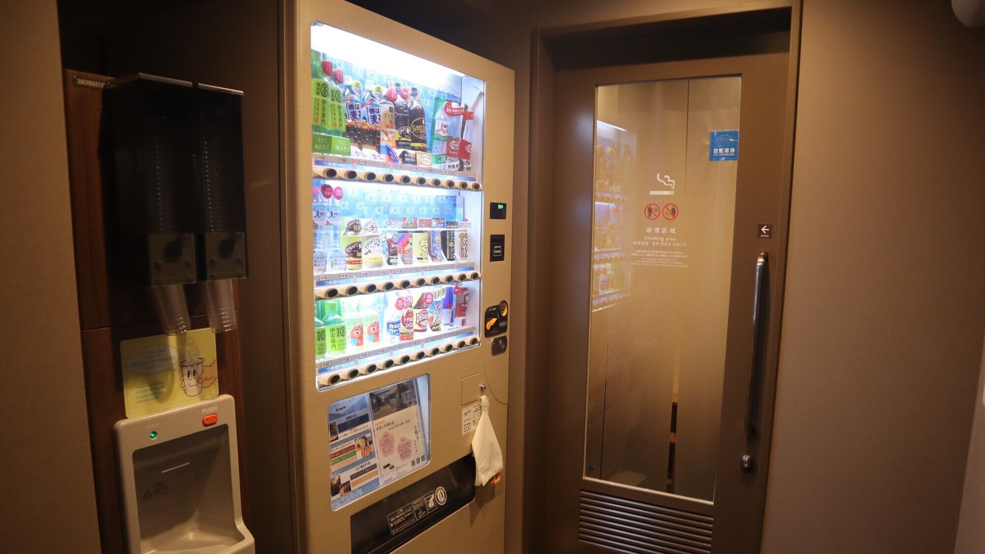 A vending machine with various beverages and snacks, a water dispenser, and a door with a smoking area sign.