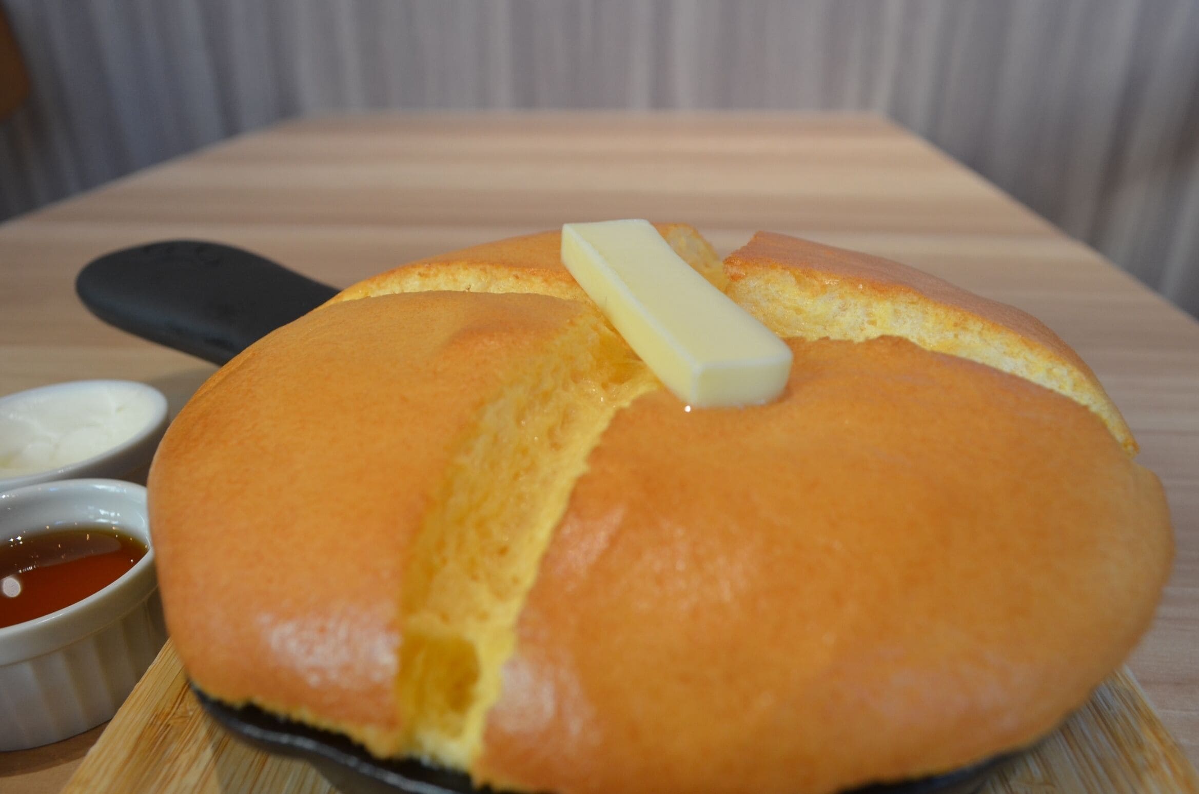 A round bread with a butter knife on a wooden board, accompanied by two small bowls of dipping sauces.