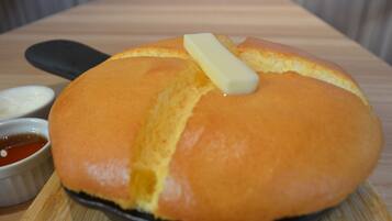 A round bread with a butter knife on a wooden board, accompanied by two small bowls of dipping sauces.