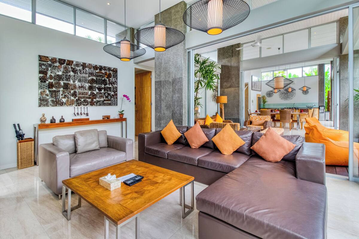 A spacious living area with a large sectional sofa, a wooden coffee table, and a wall-mounted abstract art piece.