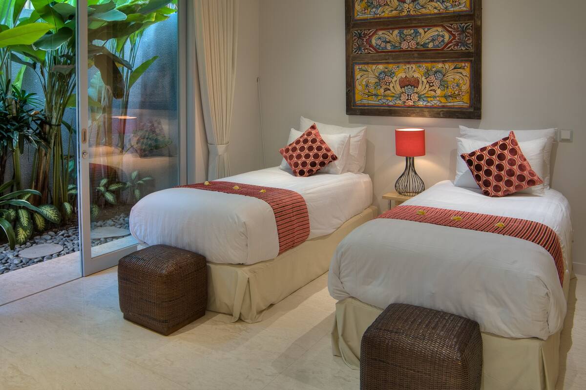 A hotel room with two beds, a glass door leading to a garden, and decorative wall art.