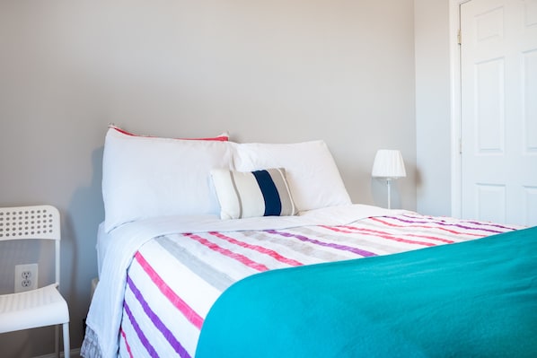 A neatly made bed with a striped bedspread, a white chair, and a white lamp beside the bed.