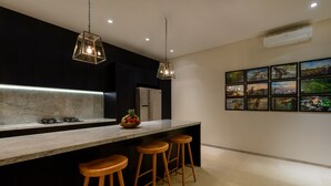 A modern kitchen with a marble countertop, stainless steel appliances, wooden bar stools, pendant lighting, and a wall of framed artwork. - Villa The Maya (Canggu)