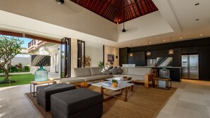A spacious living area with a modern sofa, coffee table, and a kitchen area with a refrigerator and cabinets. - Villa The Maya (Canggu)